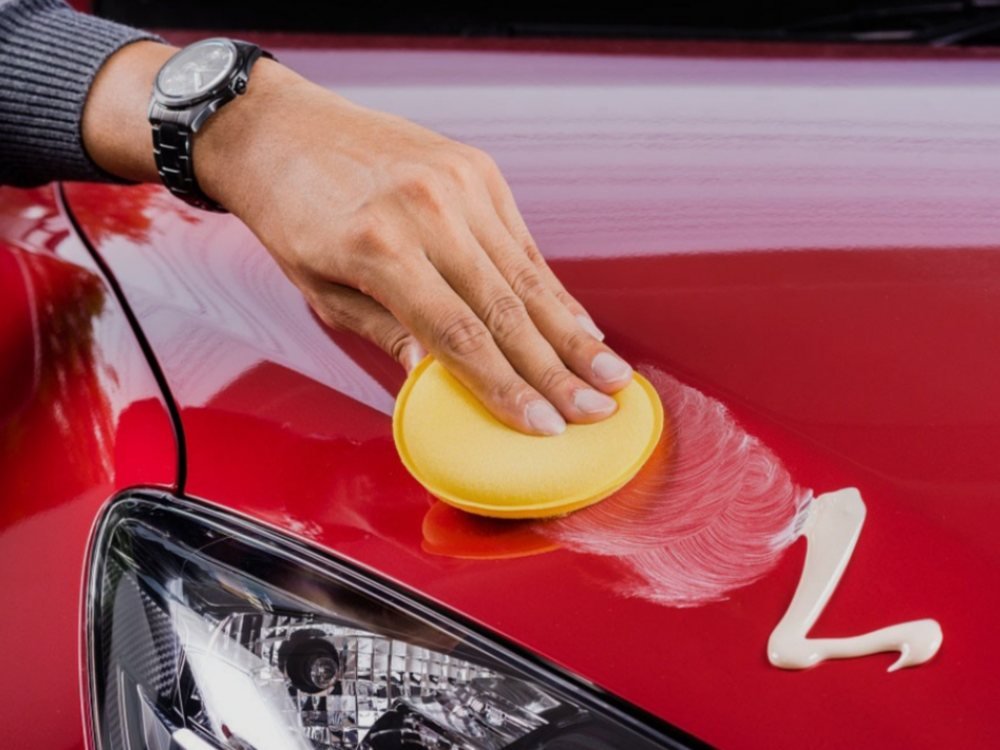 Aplicação de cera automotiva com aplicador de espuma no capô de um carro